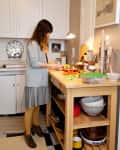 Woman chopping vegetables on a wooden kitchen island with shelves, surrounded by kitchenware and decor.