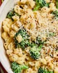 Creamy pasta with broccoli, topped with grated cheese and red pepper flakes in a bowl.