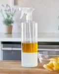 Spray bottle with yellow liquid and bowl of lemon wedges on kitchen counter.