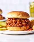 A sloppy Joe's sandwich on a hamburger bun on a plate with pickles