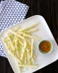 Jicama sticks on a white plate with lime zest and a small bowl of dipping sauce, next to a blue polka dot napkin.