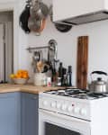 Cozy kitchen with blue cabinets, wooden countertop, hanging pots, and a kettle on the stove.