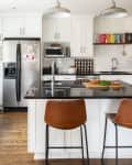 Modern kitchen with white cabinets, black countertops, brown bar stools, and a wooden dining table with a plant.
