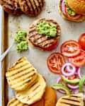 Turkey avocado burgers, with grilled turkey patties, mashed avocados, sliced tomatoes, red onions, and grilled buns on a sheet pan