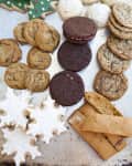 Assorted holiday cookies including gingerbread trees, snowflakes, chocolate sandwich cookies, and biscotti on a tray.