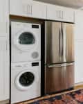 Laundry area with stacked washer and dryer next to stainless steel fridge, adjacent to dining table with flowers.