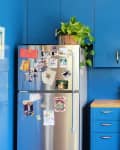 Blue kitchen with stainless steel fridge covered in photos, gas stove, and wooden countertop with white flowers in a vase.