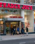 People walking past a Trader Joe's storefront with large red signage and glass windows.