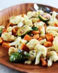 Roasted cauliflower, sweet potatoes, and Brussels sprouts on a wooden plate.