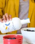 Person pouring Brightland olive oil over blueberries in a white bowl.