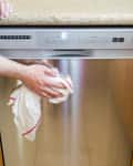 Person cleaning stainless steel dishwasher with a cloth.