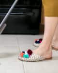 Person mopping a tiled kitchen floor wearing slippers with colorful pom-poms.