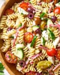Pasta salad with cherry tomatoes, chopped cucumbers, red onions, olives, and other ingredients in a wooden bowl