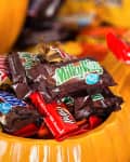 Assorted candy bars in a carved pumpkin, including Milky Way, Snickers, and Twix, with a festive Halloween theme.