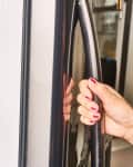 Hand with red nails opening a freezer door, revealing ice cream, frozen vegetables, and packaged food inside.