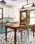 Kitchen with green lower cabinets, white upper cabinets, wooden table, metal stools, and geometric patterned floor tiles.