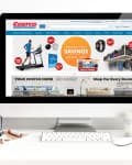Computer screen displaying Costco website with home delivery options, treadmill, and member savings. Desk with flowers and stationery.