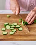 Someone slices the cucumber on a wooden chopping board