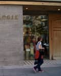 Storefront of Anthropologie with a woman walking by, wearing a white shirt and red jacket tied around her waist.