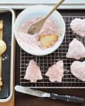 Heart and tree-shaped pastries on a baking sheet and cooling rack, with a bowl of pink sugar mixture and a spatula.