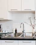 A stainless steel sink is shown in a white kitchen