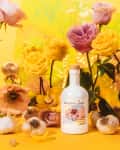Brightland olive oil bottle surrounded by pink and yellow roses, garlic, and decorative vases on a vibrant yellow background.