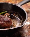Seared steak in a cast iron skillet with rosemary garnish.