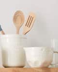 Ceramic kitchen utensils set with wooden spoons and spatula on a wooden countertop.