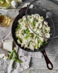 Tortellini with snap peas and grated cheese in a skillet on a wooden table, accompanied by a glass of white wine.