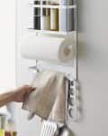 Wall-mounted kitchen organizer with paper towel holder, spice jars, aluminum foil, and utensils hanging below.