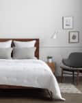 Modern bedroom with wooden bed, white bedding, gray pillows, side tables, lamps, and minimalist wall art.