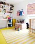 Bright children's room with colorful bookshelves, patterned bed, striped rug, and wooden crib.