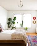 Bedroom with a wooden bed, colorful rug, large plant, and horse artwork above a dresser.