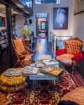 Eclectic living room with leather chairs, colorful cushions, books on a glass coffee table, and art on the walls.