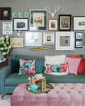 Living room with teal sofa, colorful pillows, pink ottoman, gallery wall, and decorative items on side tables.