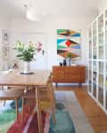 Dining room with wooden table and chairs, colorful rug, sideboard, and abstract wall art.
