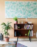 Mid-century modern living room with a wooden bookshelf, potted plants, a white bicycle, and a teal patterned wall art.