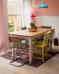 Dining room with a wooden table, mismatched chairs, fruit bowl centerpiece, red lamp, and turquoise pendant light.