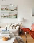 Modern living room with gray and cream sofas, orange chair, marble coffee table, and wall art above.