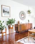 Mid-century modern living room with gray sofa, wooden coffee table, sideboard, plants, and wall art.