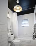 A bathroom with subway tile walls, penny tile flooring, and a black ceiling