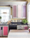 Colorful kitchen with patterned cabinet doors, black countertops, potted plants, and framed photos above the sink.