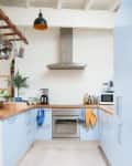 View into a narrow kitchen with light blue cabinets and a stainless steel oven and range hood