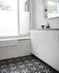 Bathroom with white subway tiles, patterned black and white floor, white cabinets, and a large window.