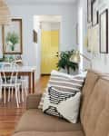 Brown sofa with striped pillows, gold lamp, dining table with white chairs, and a yellow door in the background.