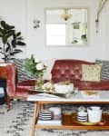 Velvet pink sofa with patterned cushions, marble coffee table, plants, and decorative mirrors in a cozy living room.
