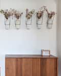 Hallway with wooden cabinet, wall-mounted vases holding dried flowers, and a mail holder on top.