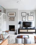 Modern living room with a TV, gallery wall, beige sofa, and armchair near a staircase.