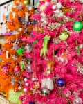 Colorful Christmas trees with pink, orange, and purple tinsel, adorned with eclectic ornaments in a vibrant room.