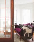 French doors open to a cozy living room with a purple sofa, decorative pillows, a horse blanket, and a potted plant.